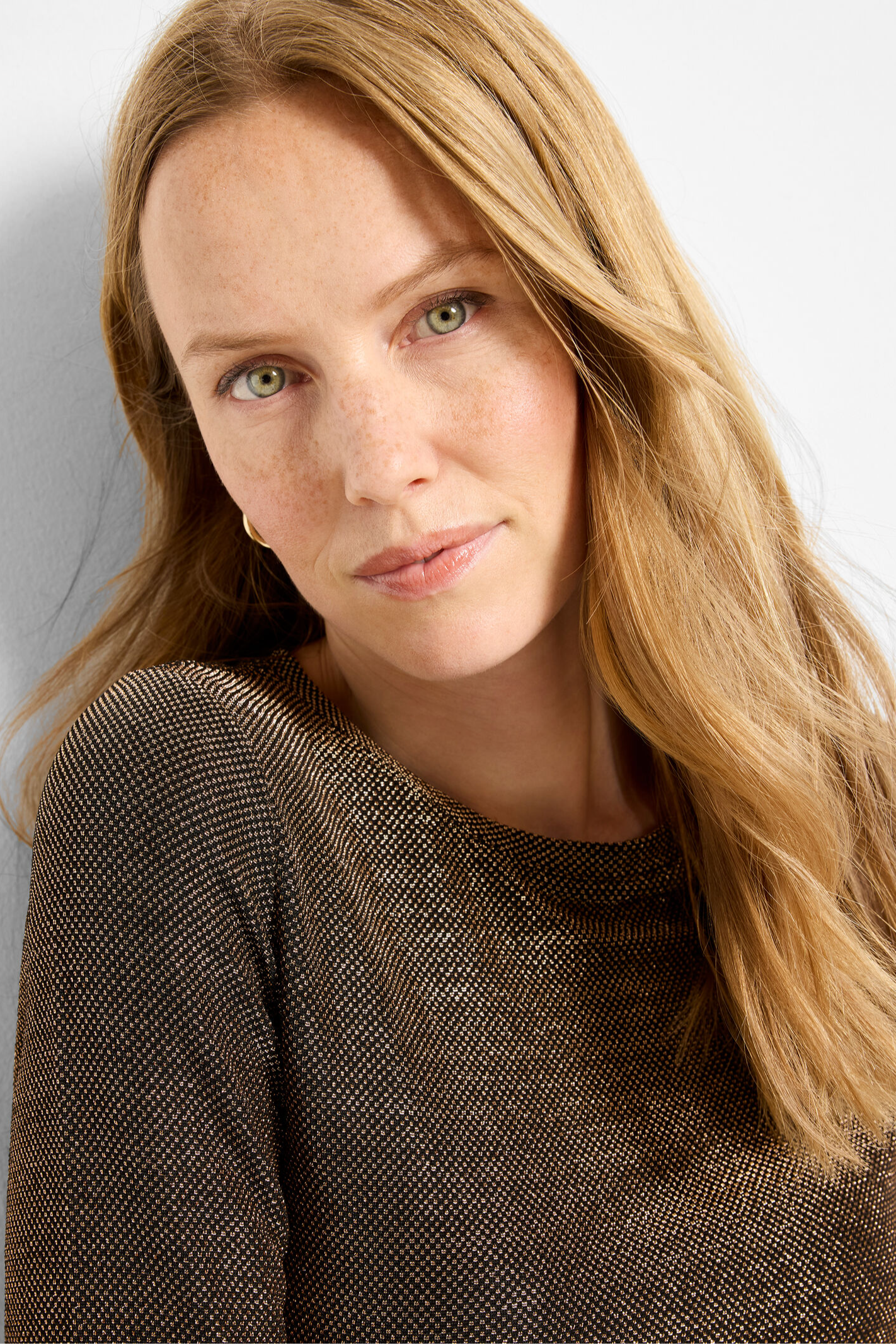 Woman with long blonde hair wearing a brown textured top against a plain background