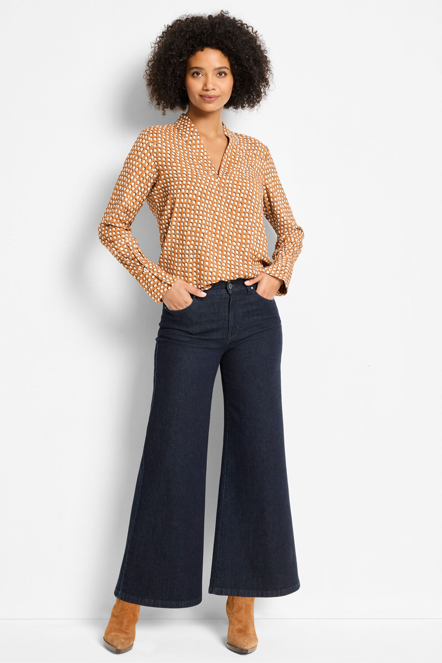 Woman wearing a patterned blouse and dark blue jeans on a white background