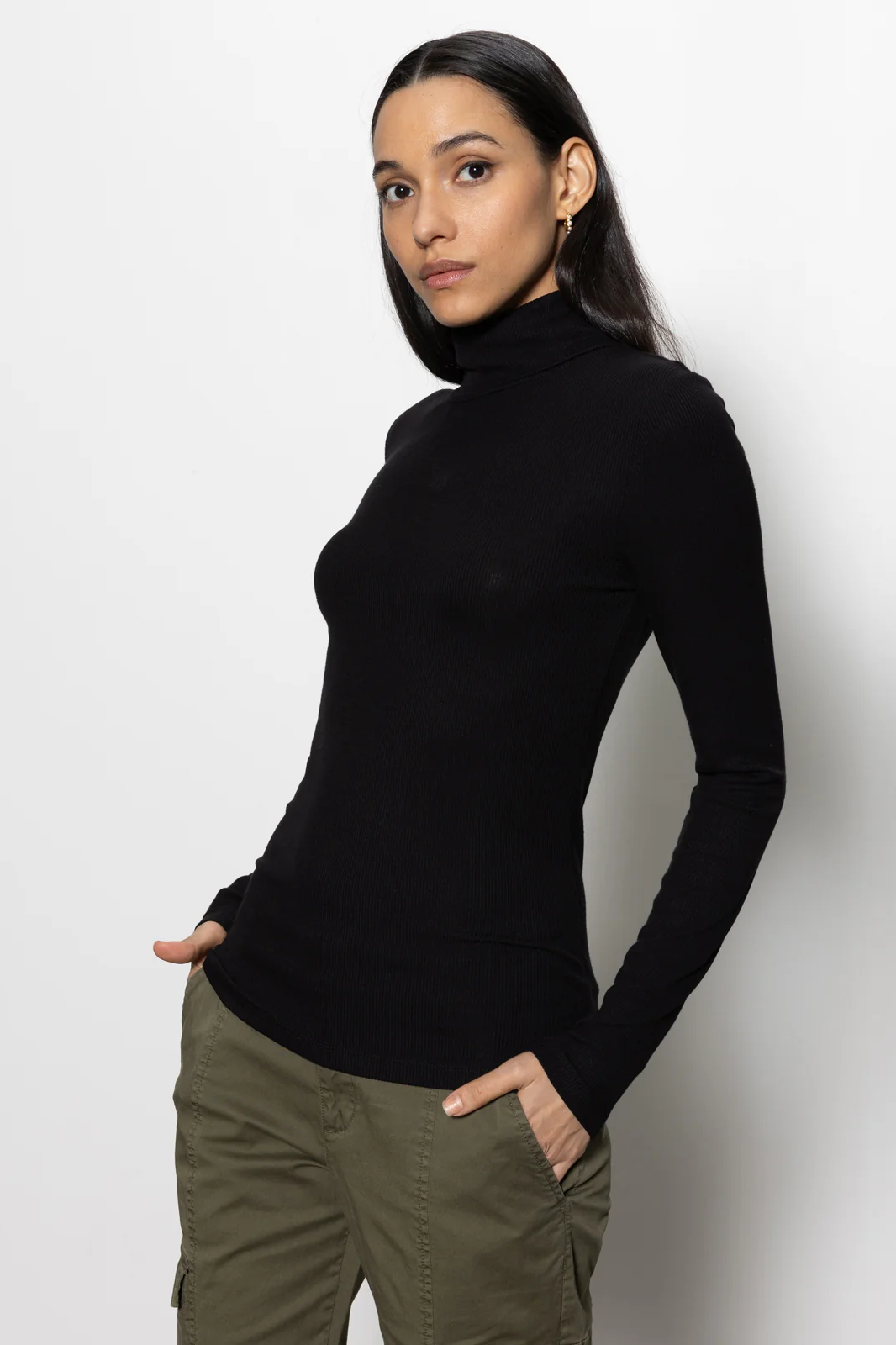 Woman wearing a black turtleneck and green pants against a white background