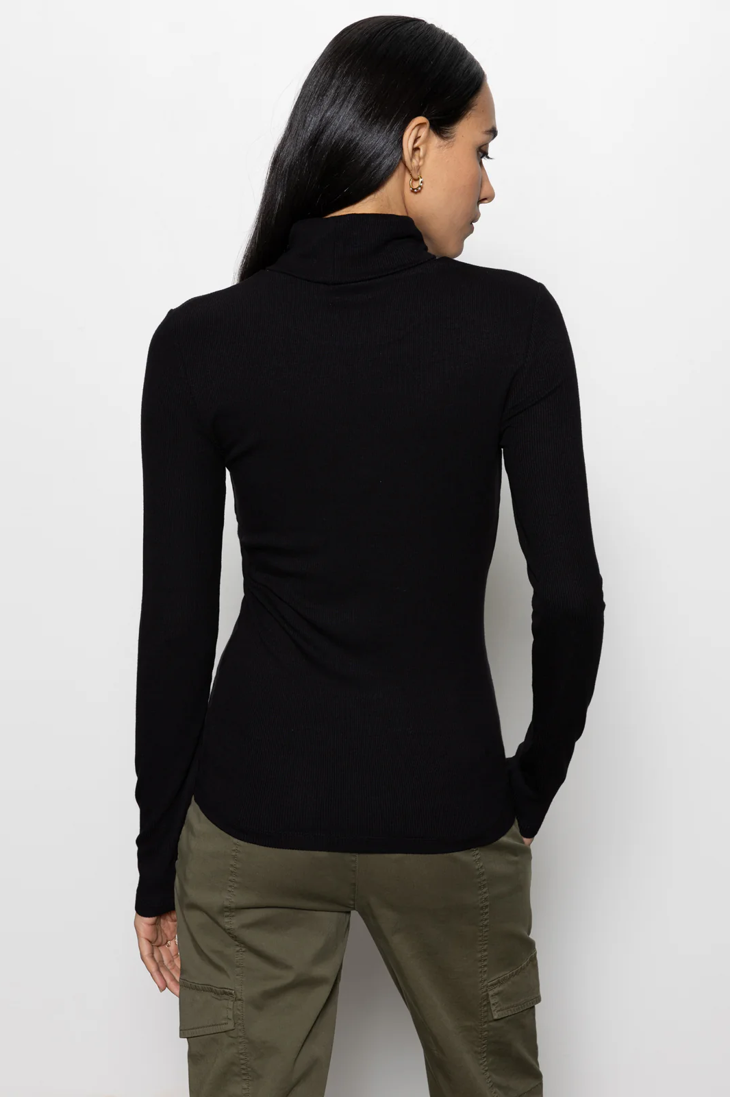Person wearing a black long-sleeve top and green pants on a white background