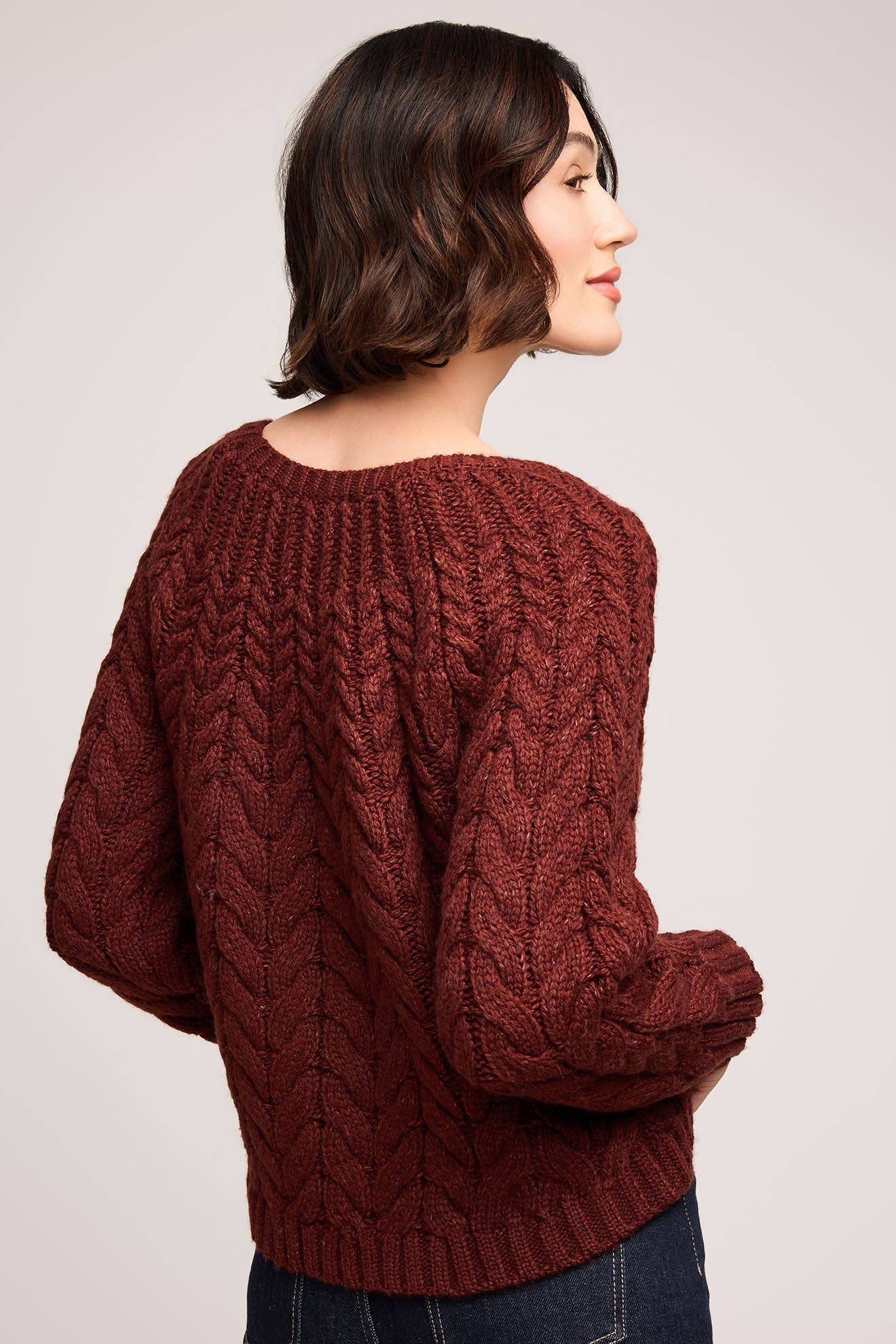 Woman wearing a brown cable knit sweater on a plain background