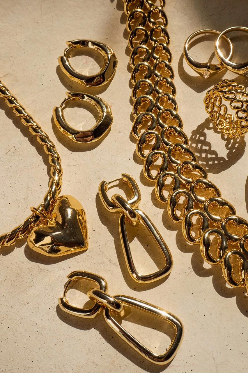 Gold jewelry including chains, rings, and pendants on a beige background