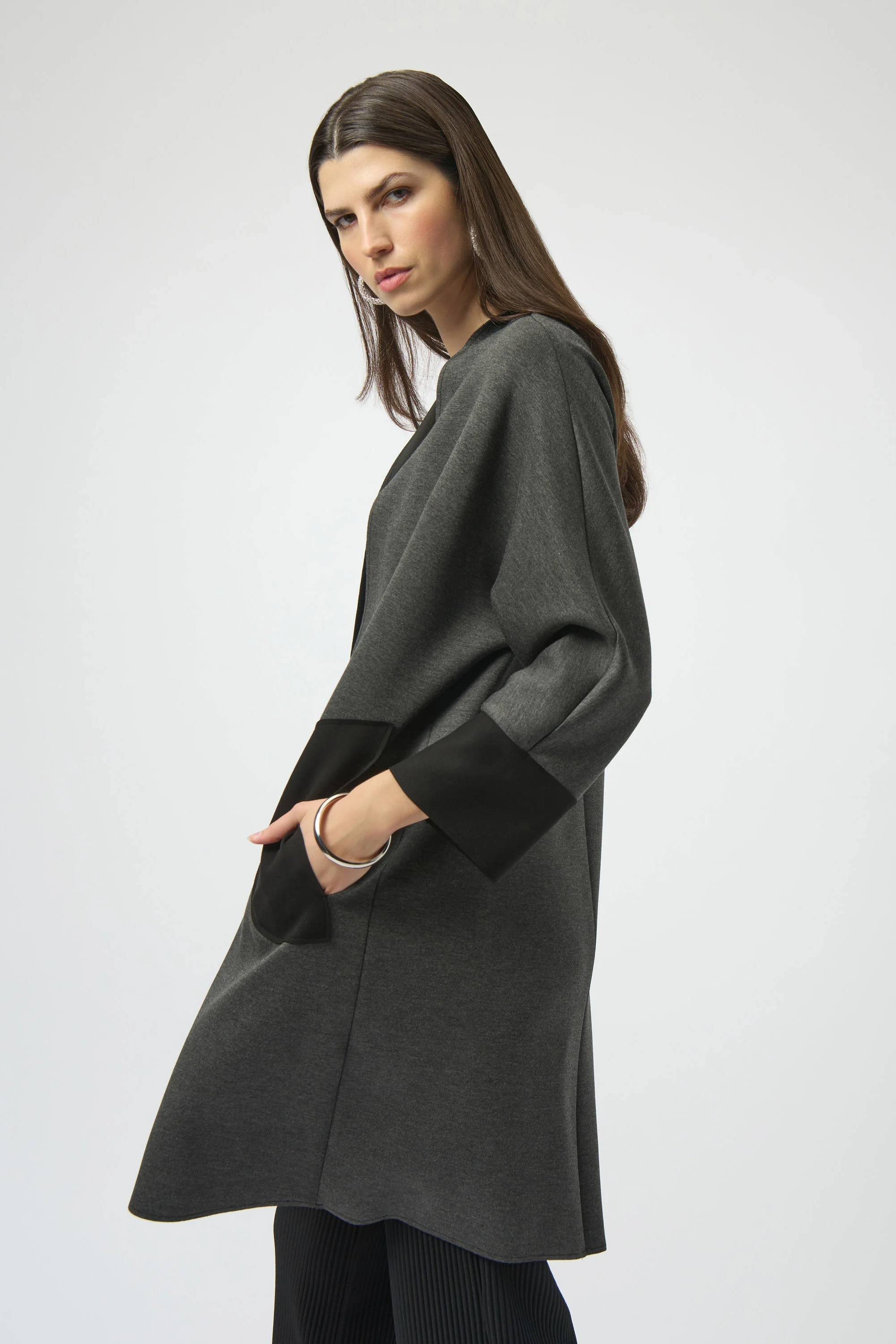 Woman wearing a dark gray poncho over a black outfit on a white background