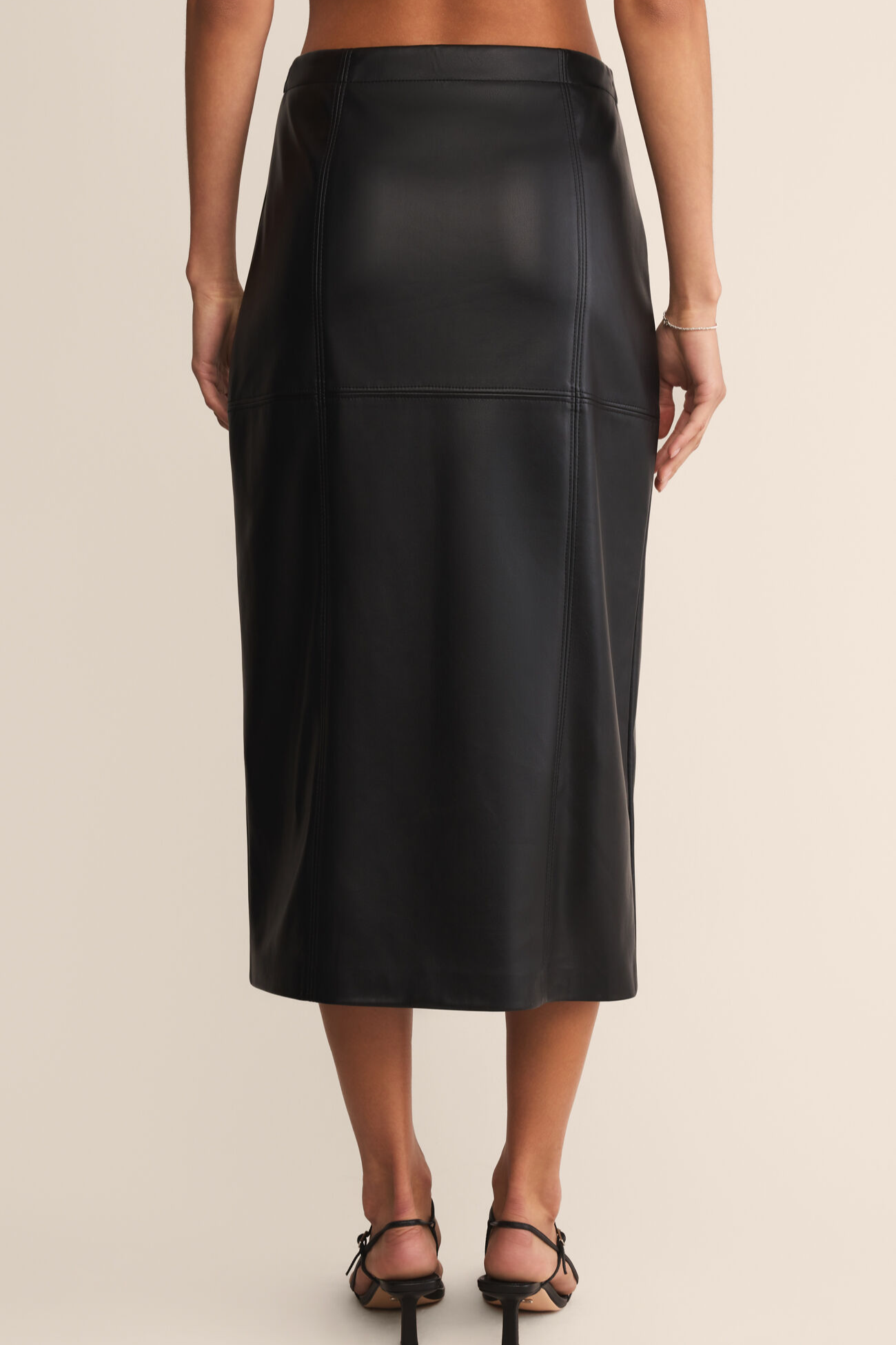 Black leather skirt worn by a person on a beige background