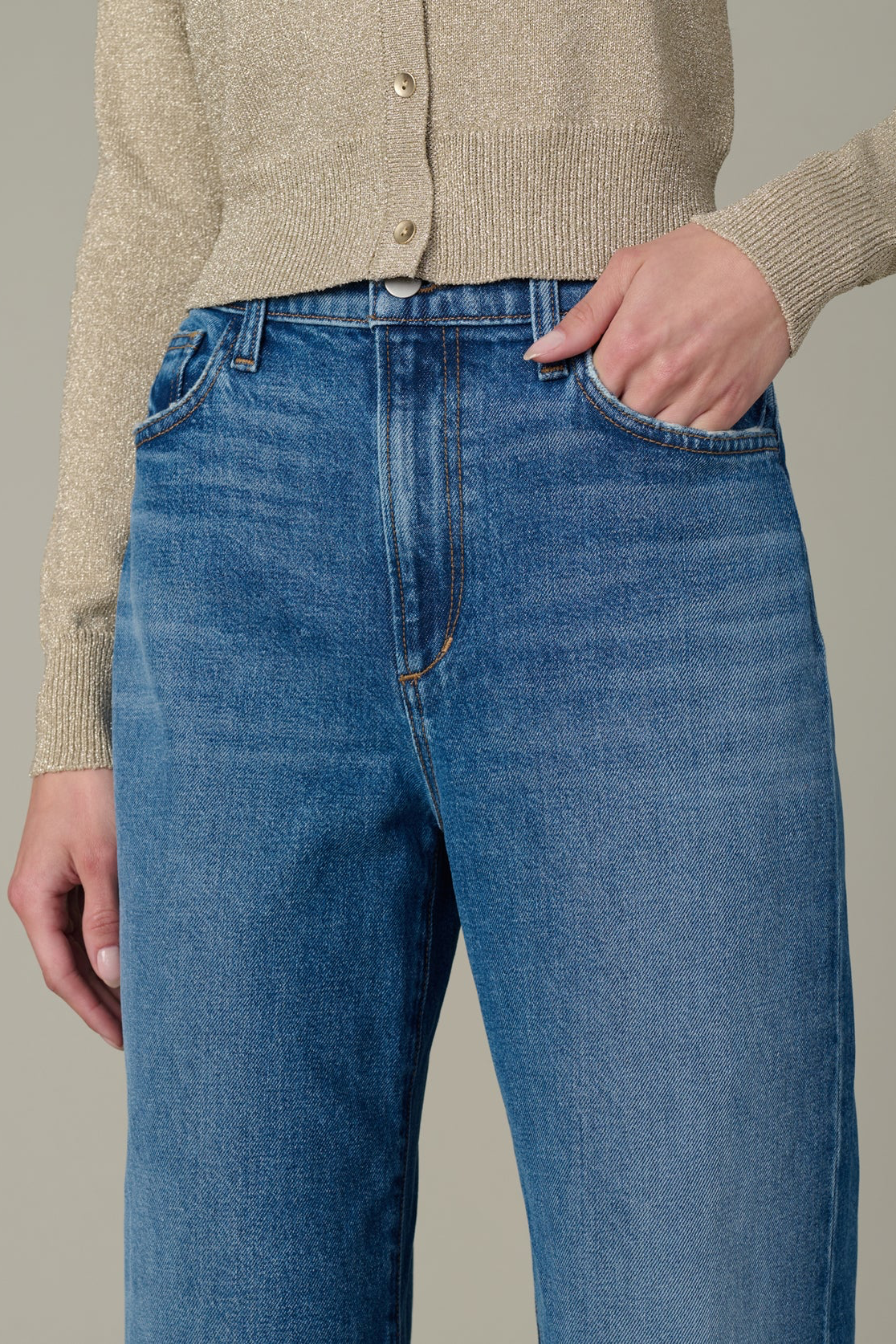 Person wearing blue jeans and a beige cardigan on a neutral background
