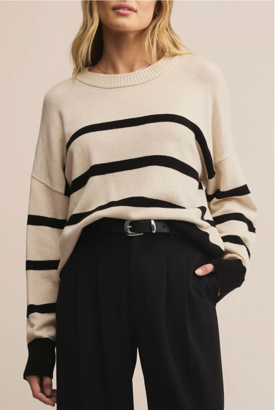Person wearing a cream sweater with black stripes and black pants on a beige background