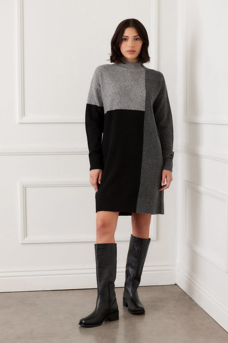 Woman wearing a black and gray dress with knee-high boots against a white wall.