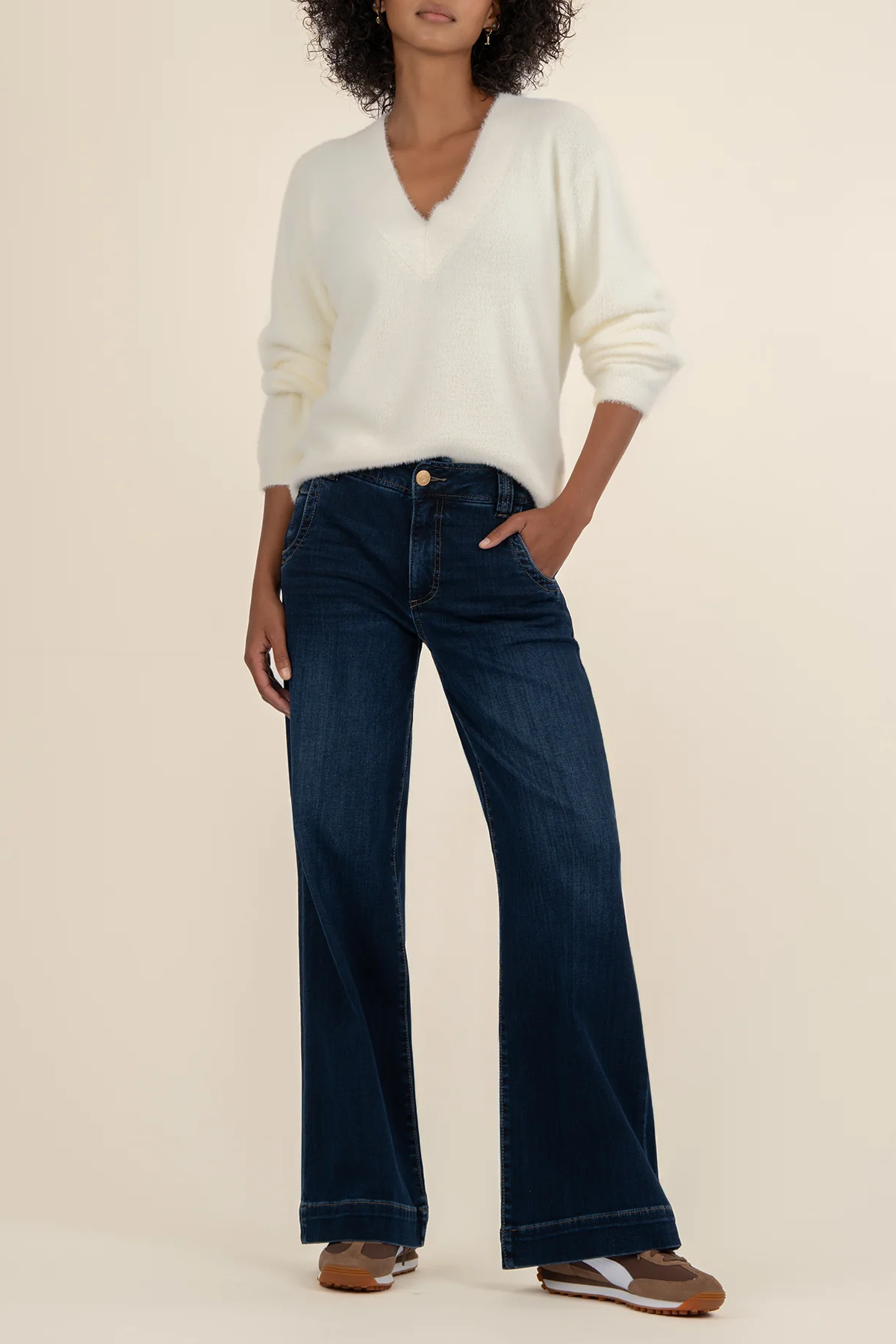 Woman wearing a white sweater and dark blue jeans on a beige background