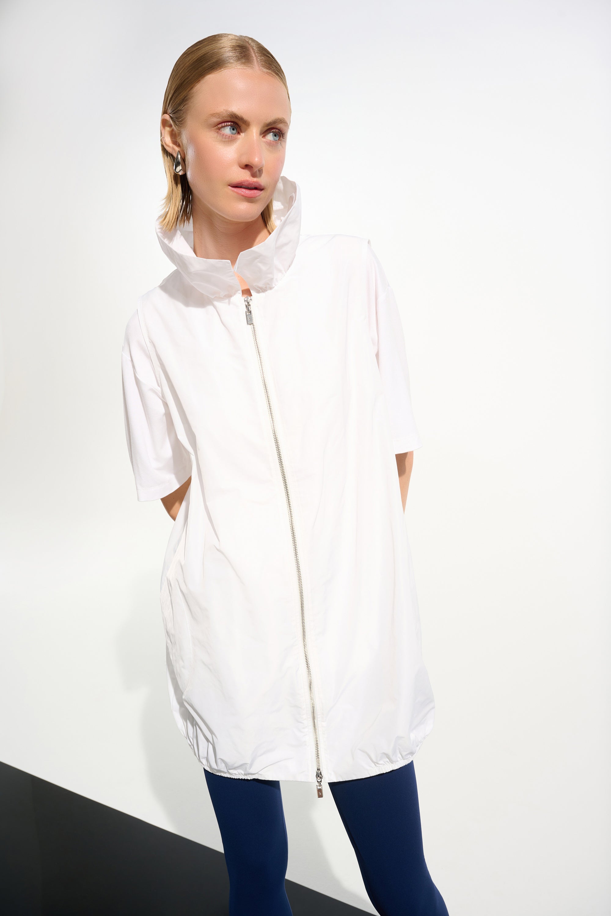 Woman wearing a white jacket with a hood on a plain background