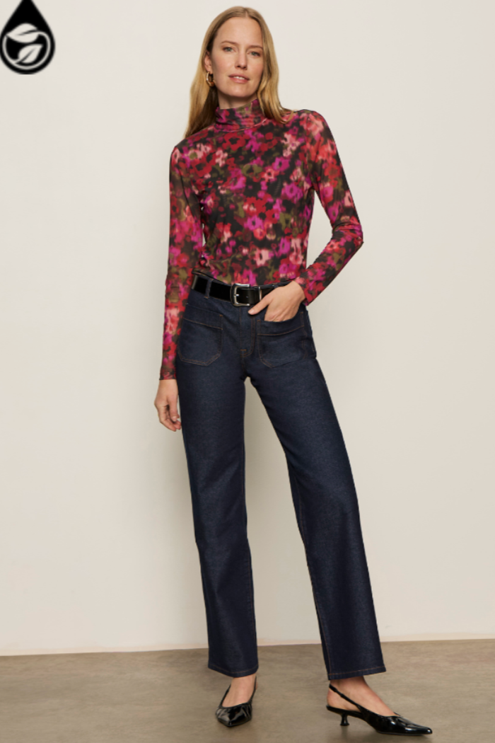Woman wearing a floral top and dark jeans against a plain background
