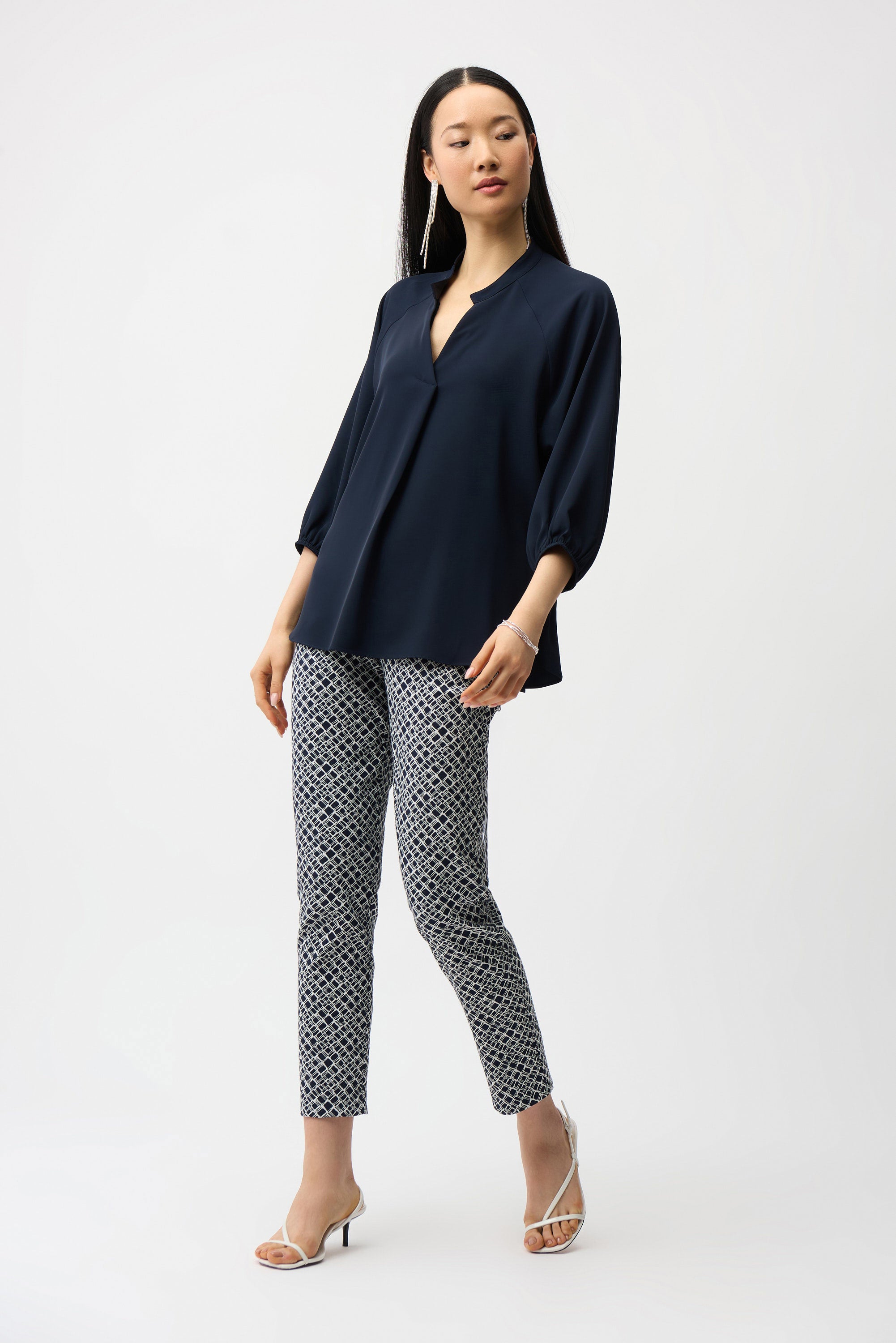 Woman wearing a navy blouse and patterned pants on a white background