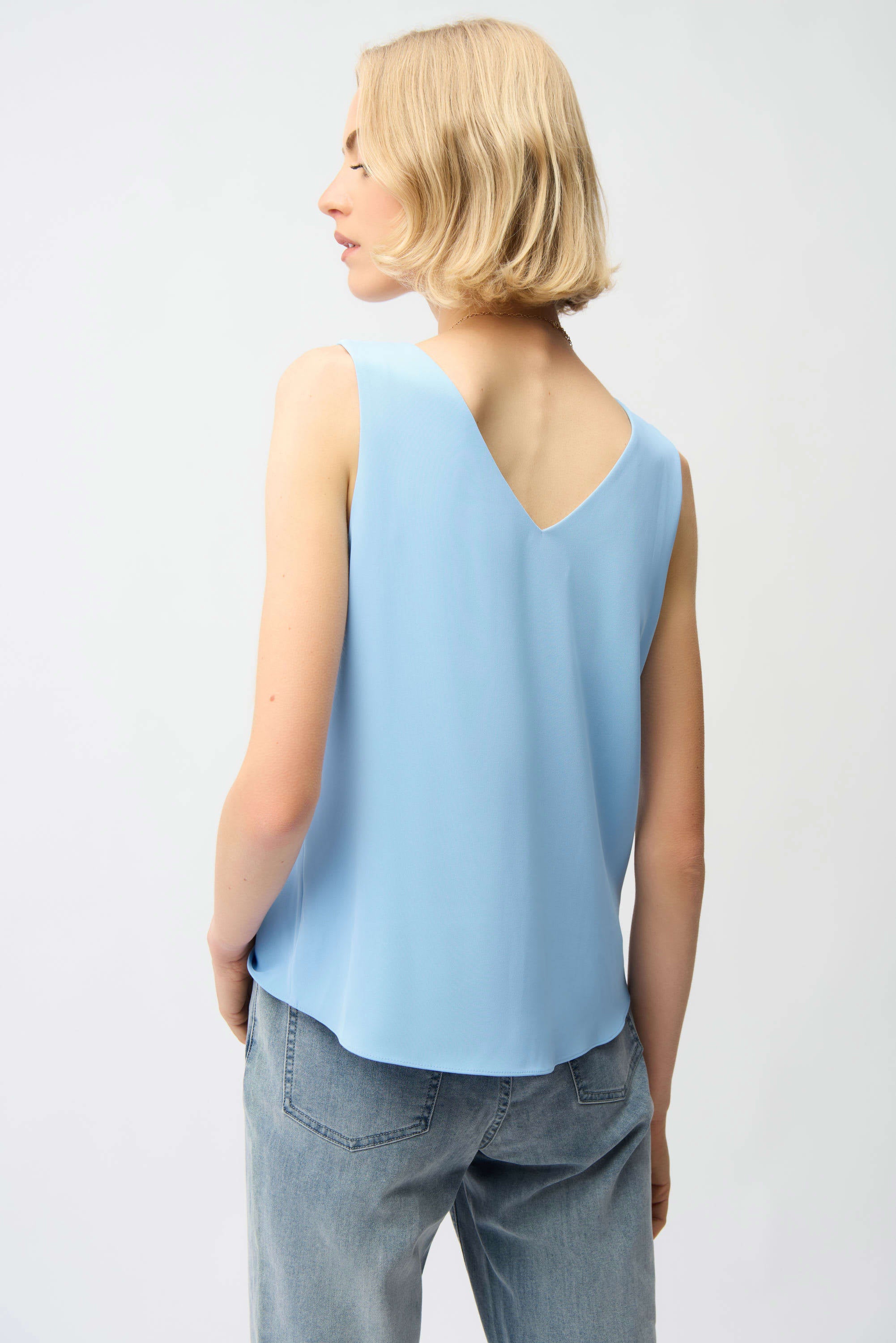 Person wearing a light blue sleeveless top and gray jeans on a white background
