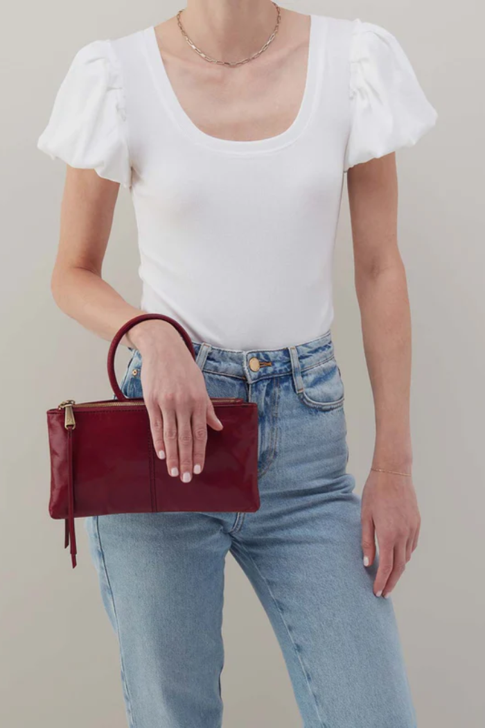 Person wearing a white top and blue jeans holding a red handbag against a neutral background
