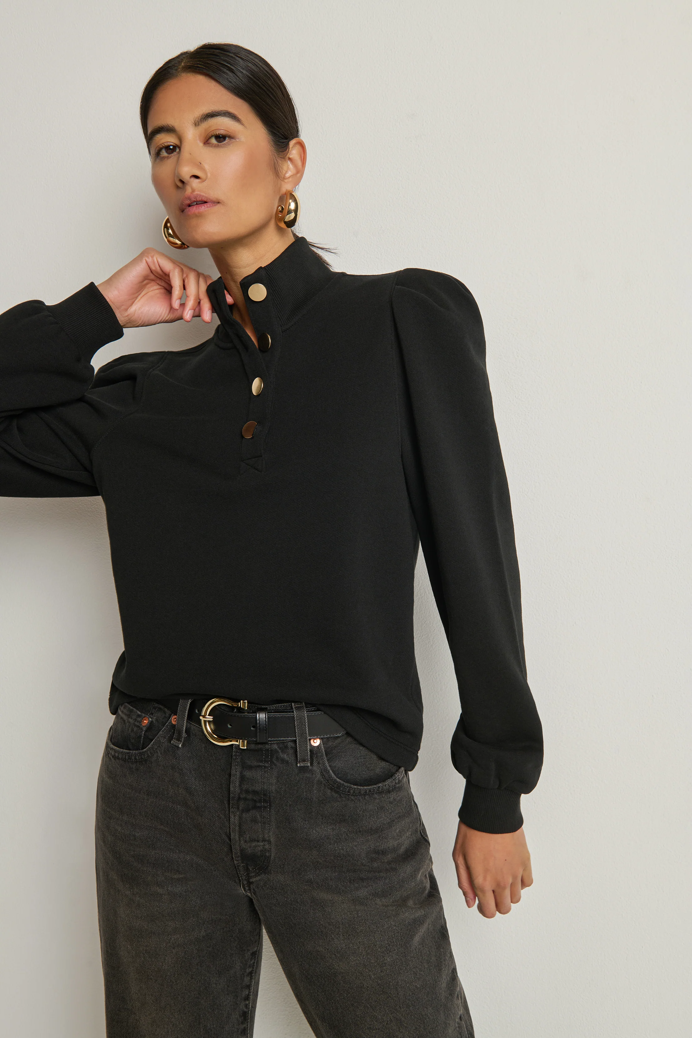 Person wearing a black blouse with long sleeves and high collar, standing against a plain background.