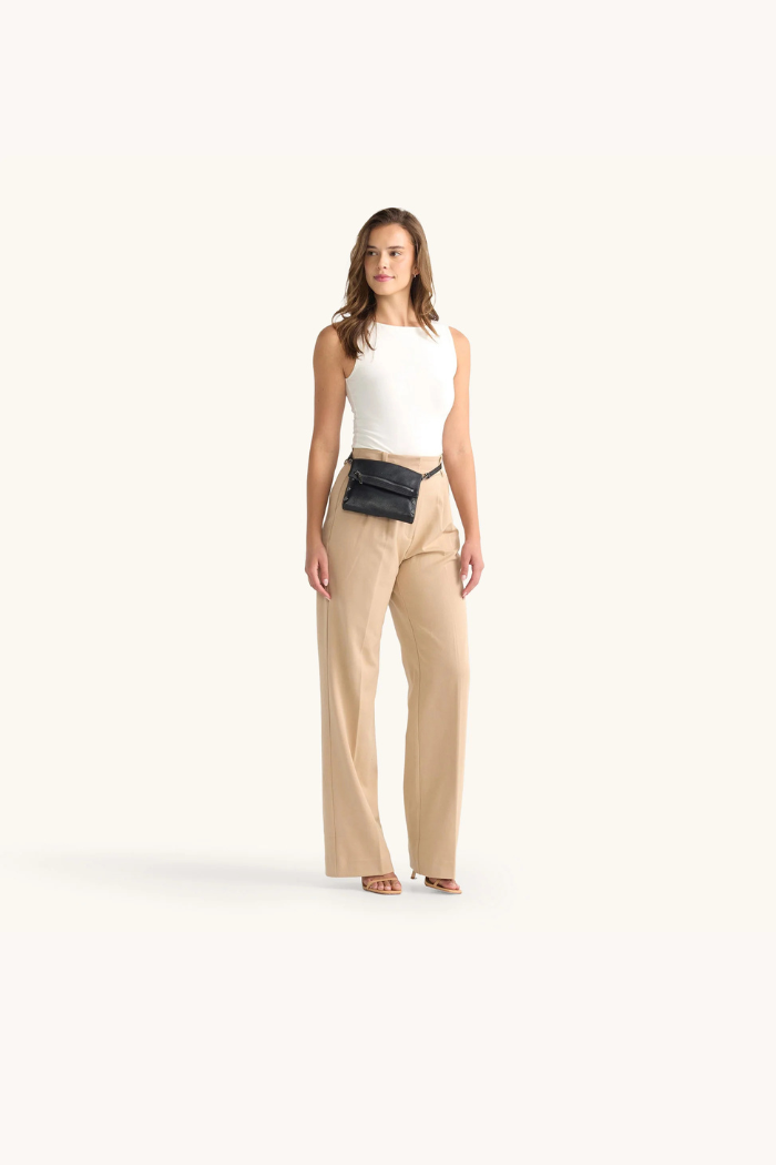 Woman wearing a white top and beige pants with a black belt bag on a white background