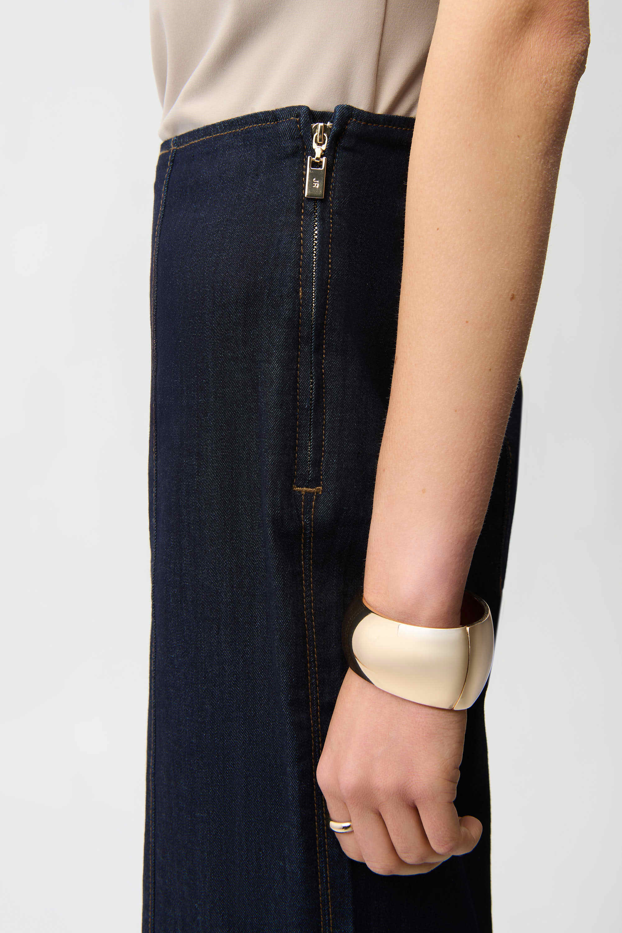 Person wearing a dark blue skirt with a zipper and a beige bracelet on a white background