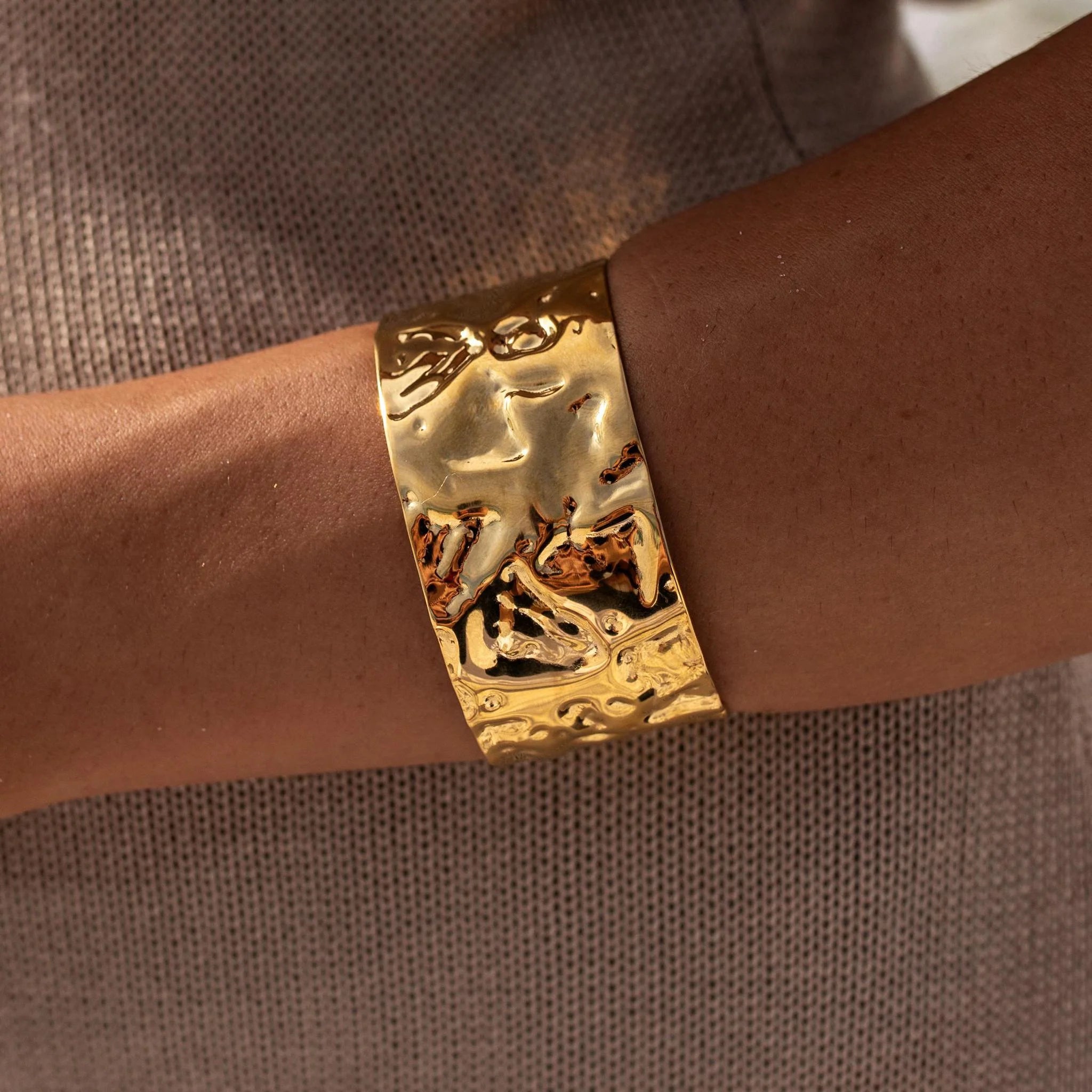 Gold bracelet with intricate design on a wrist against a brown background