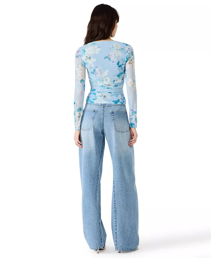 Woman wearing a light blue floral long-sleeve top and jeans on a white background