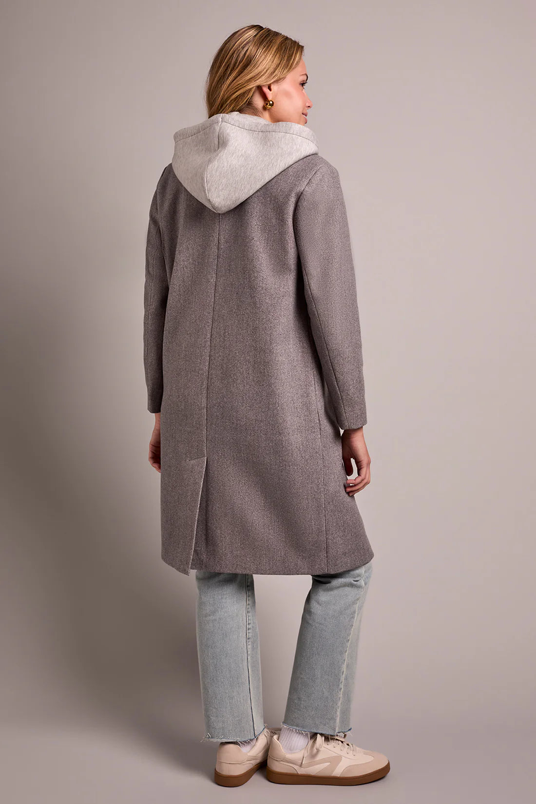 Person wearing a gray coat with a hood on a plain background