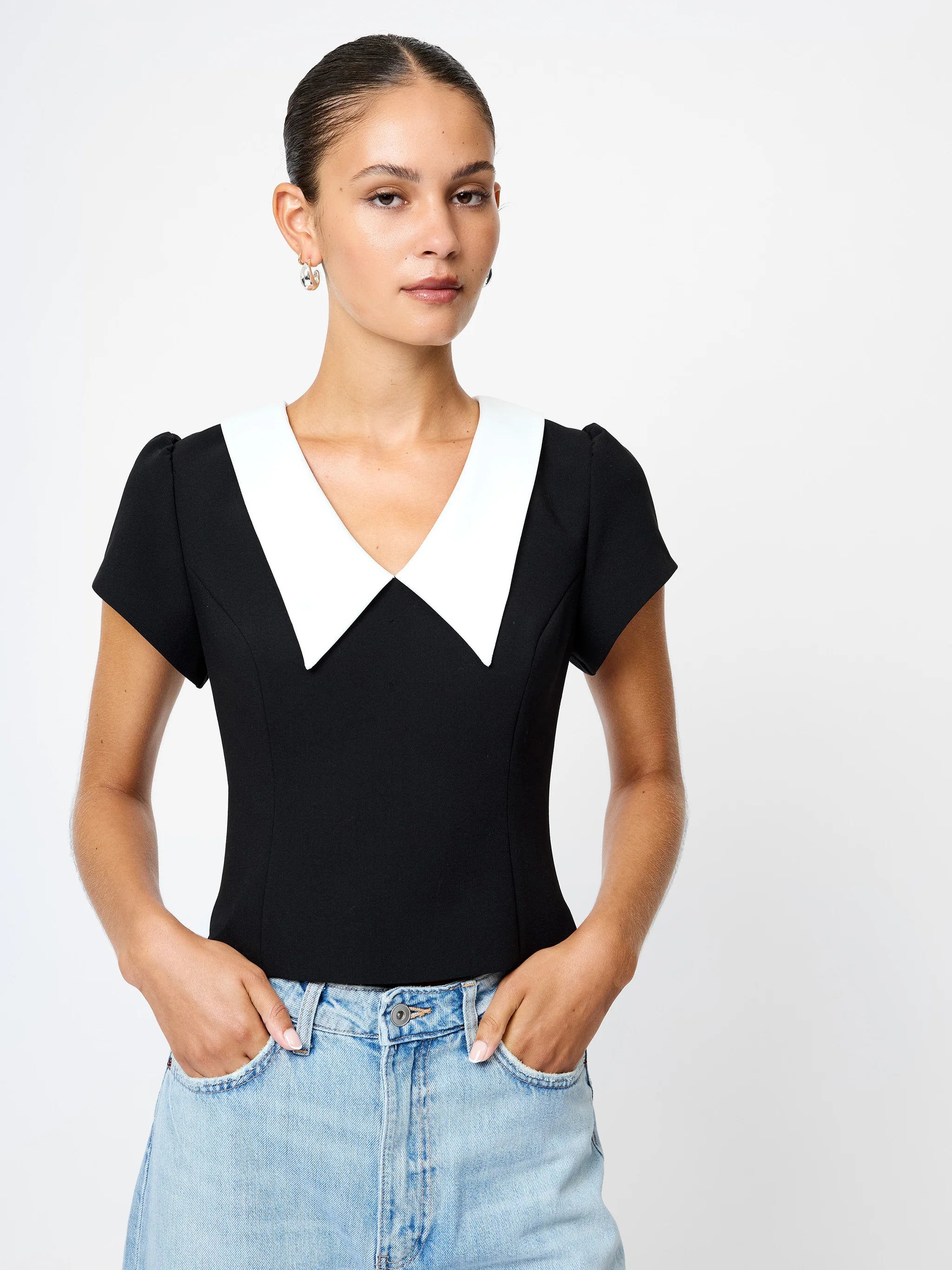 Woman wearing a black top with a white collar and blue jeans on a plain background