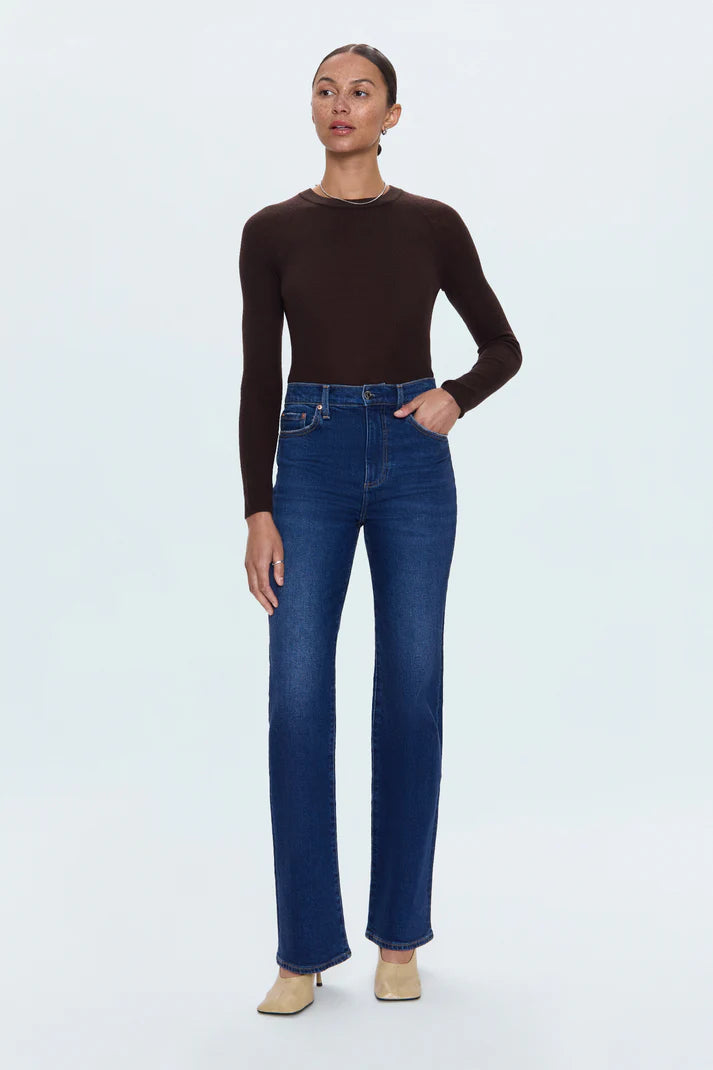 Woman wearing a brown long-sleeve top and blue jeans on a white background