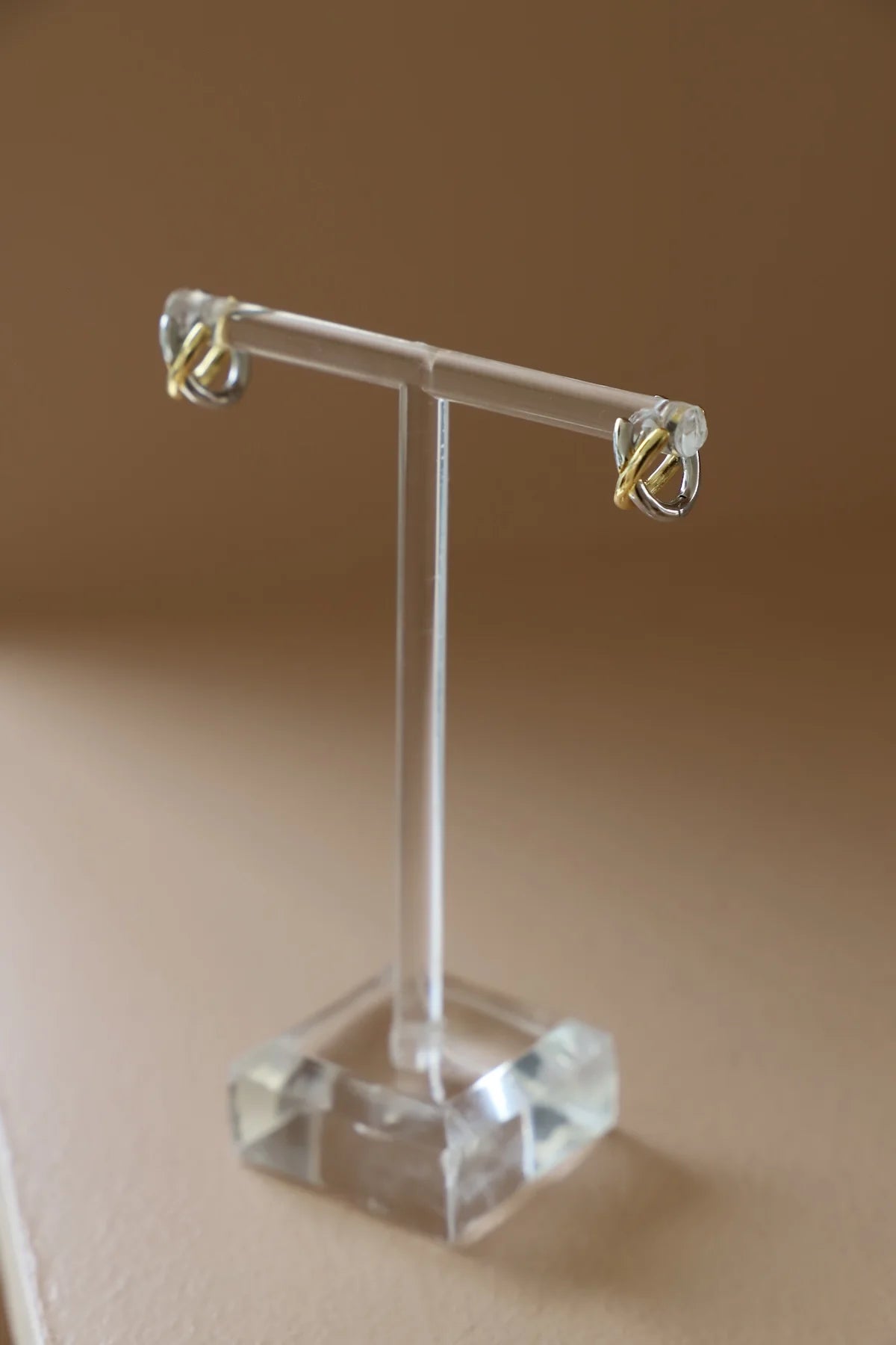 Gold earrings on a clear acrylic stand against a beige background