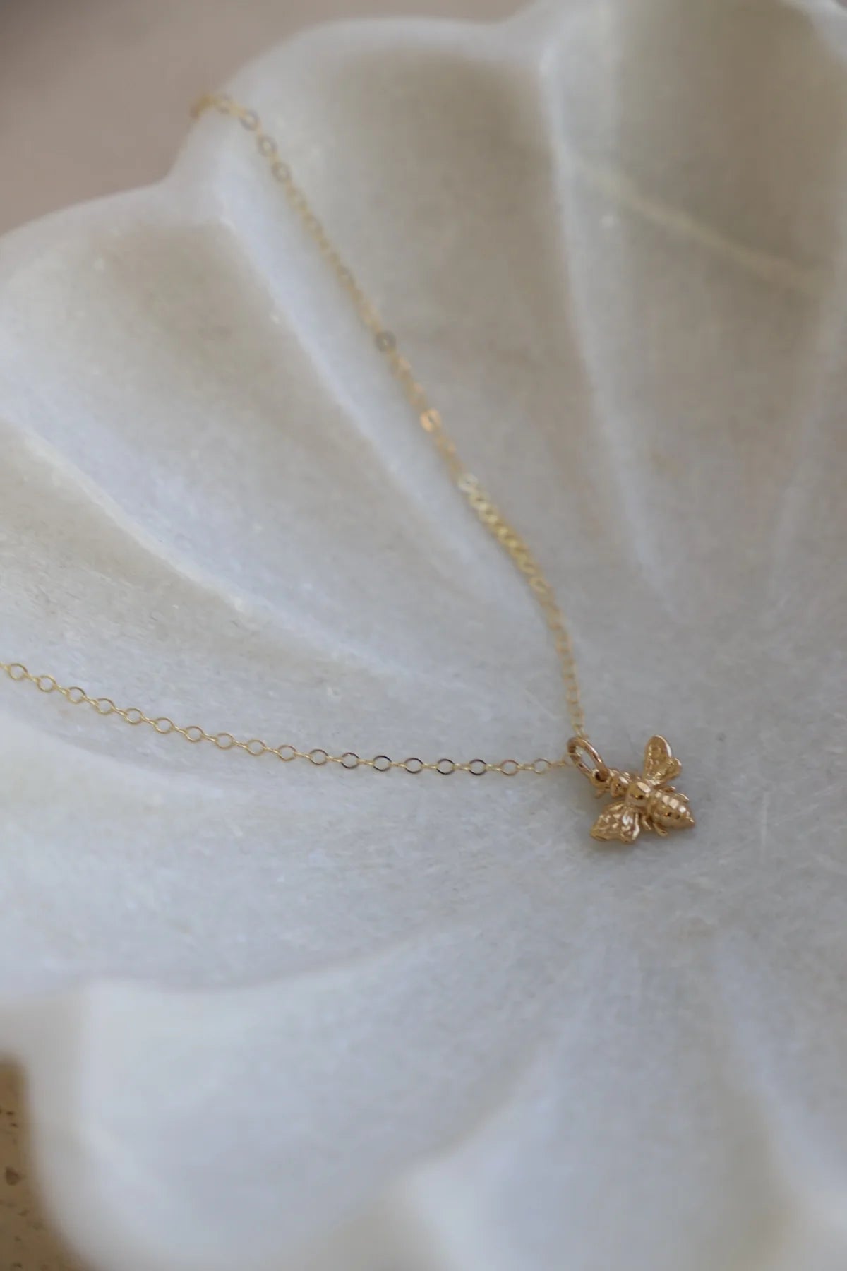 Gold necklace with a bee pendant on a white fabric background