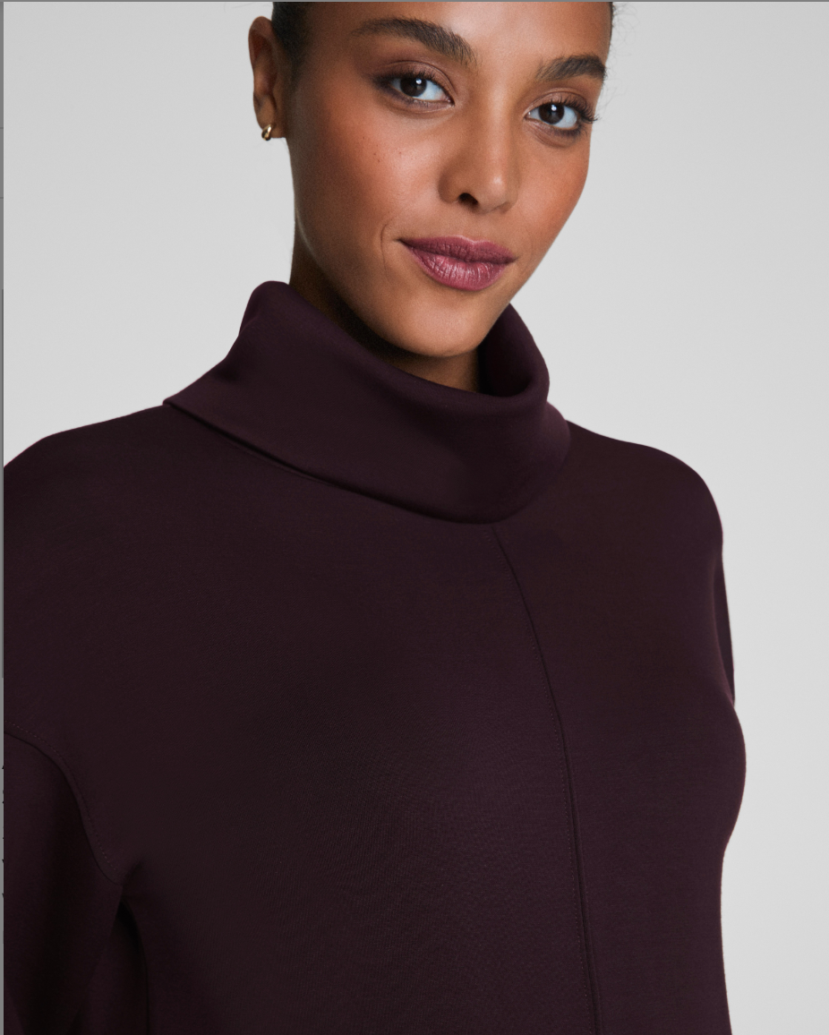 Woman wearing a dark brown turtleneck sweater against a plain background