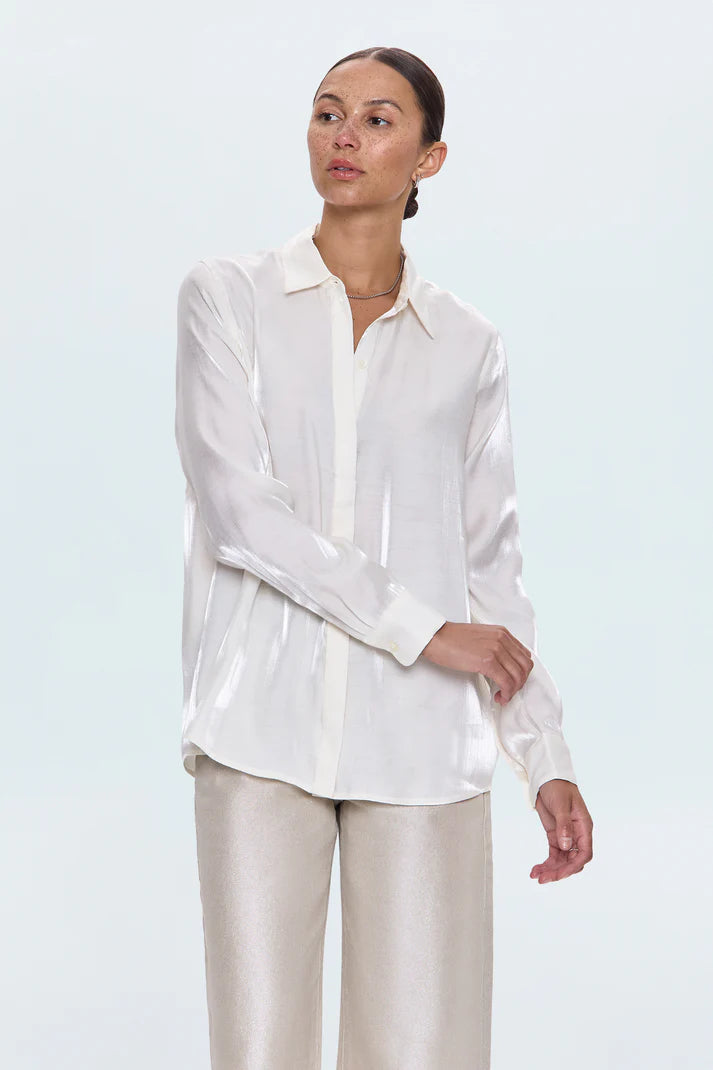 Woman wearing a white blouse and beige pants against a light blue background