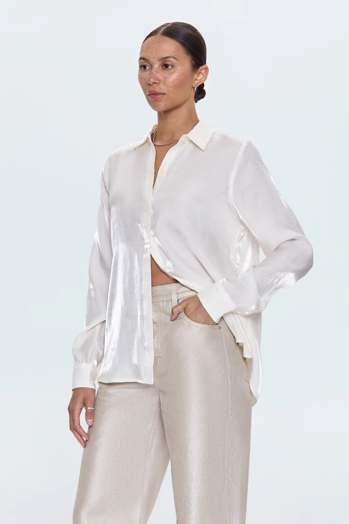 Woman wearing a white blouse and beige pants against a light blue background