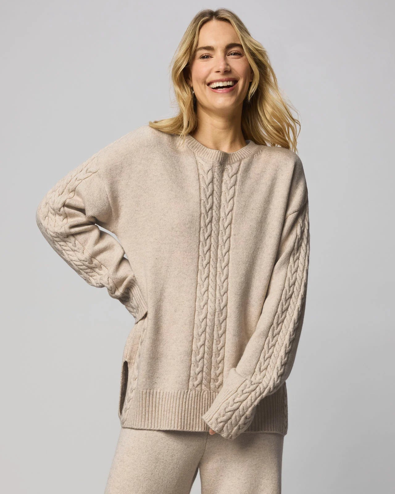 Woman wearing a beige cable knit sweater on a plain background