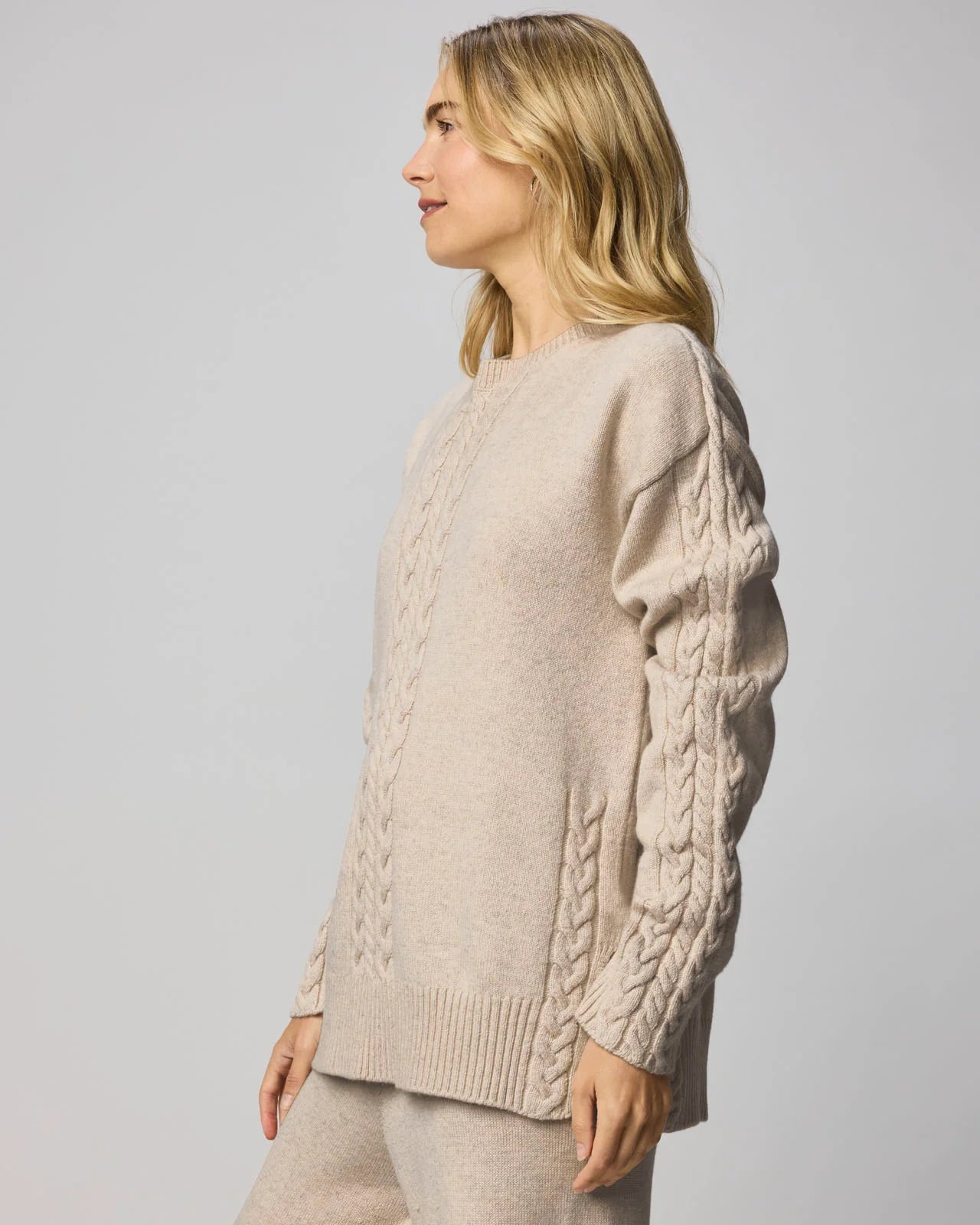 Woman wearing a beige cable knit sweater against a plain background