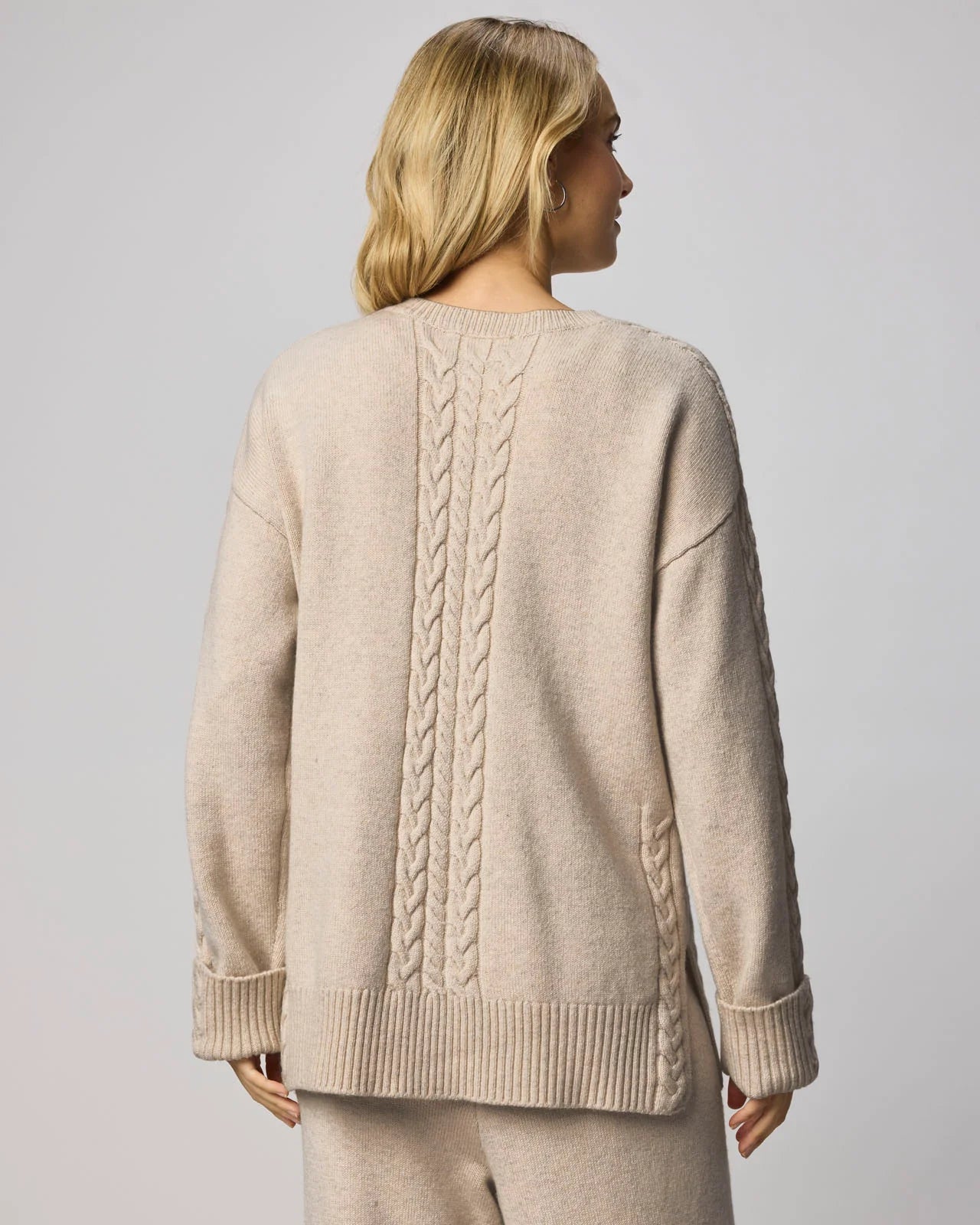 Woman wearing a beige sweater with cable knit pattern on a plain background