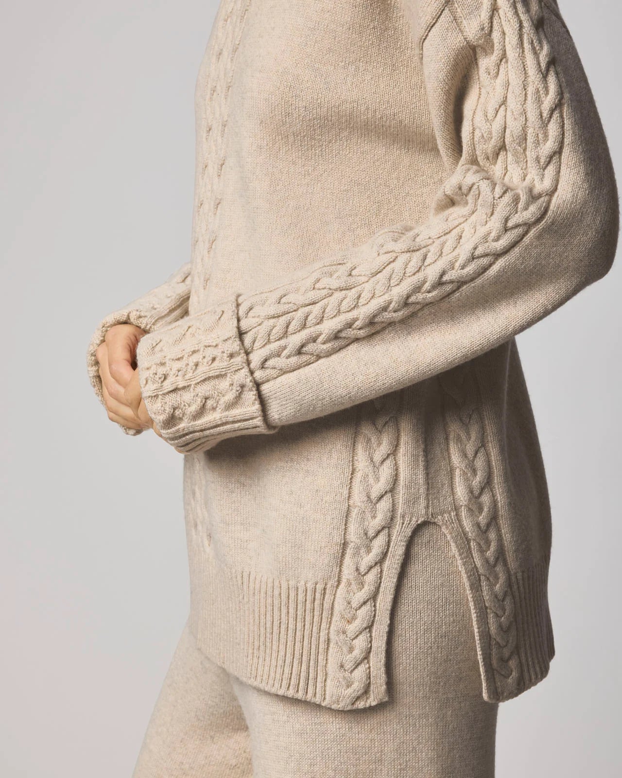 Beige cable knit sweater with detailed arm design on a light gray background