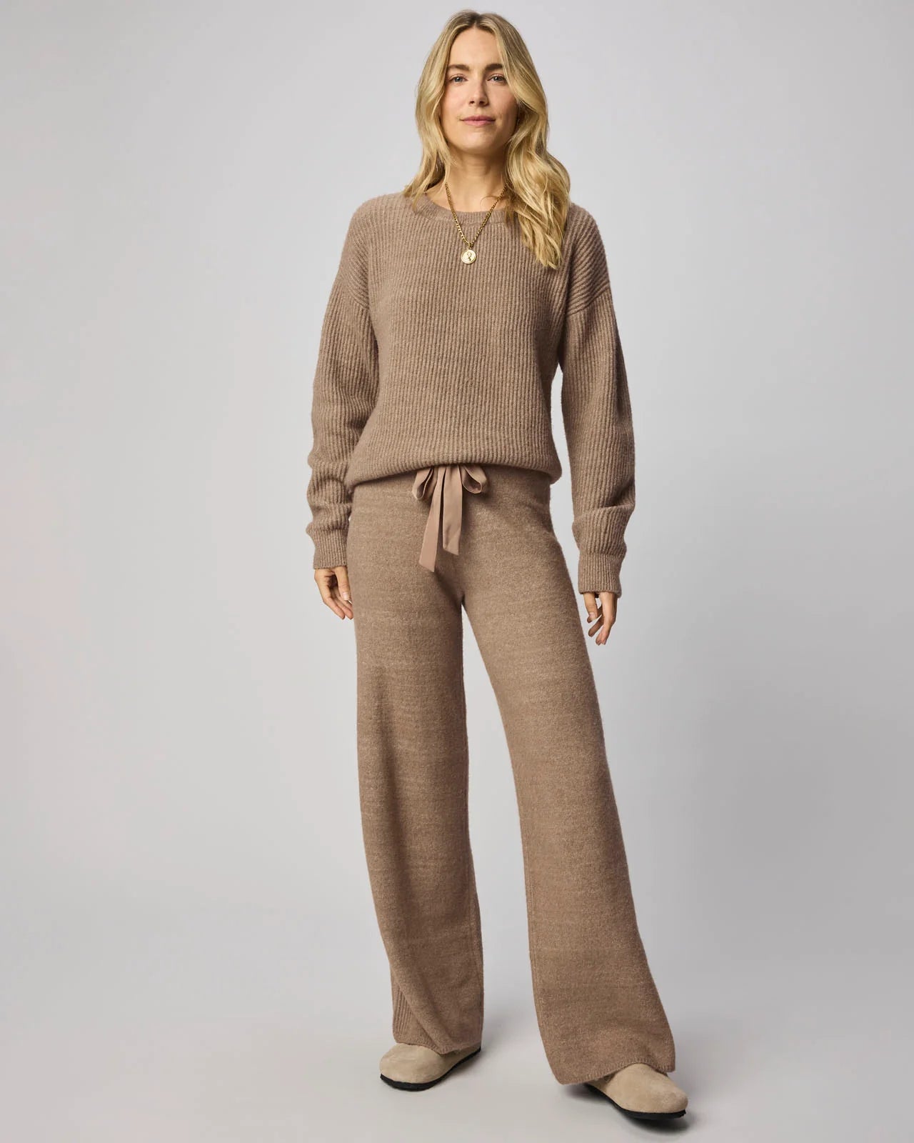 Woman wearing a brown knit outfit with a sweater and pants on a plain background