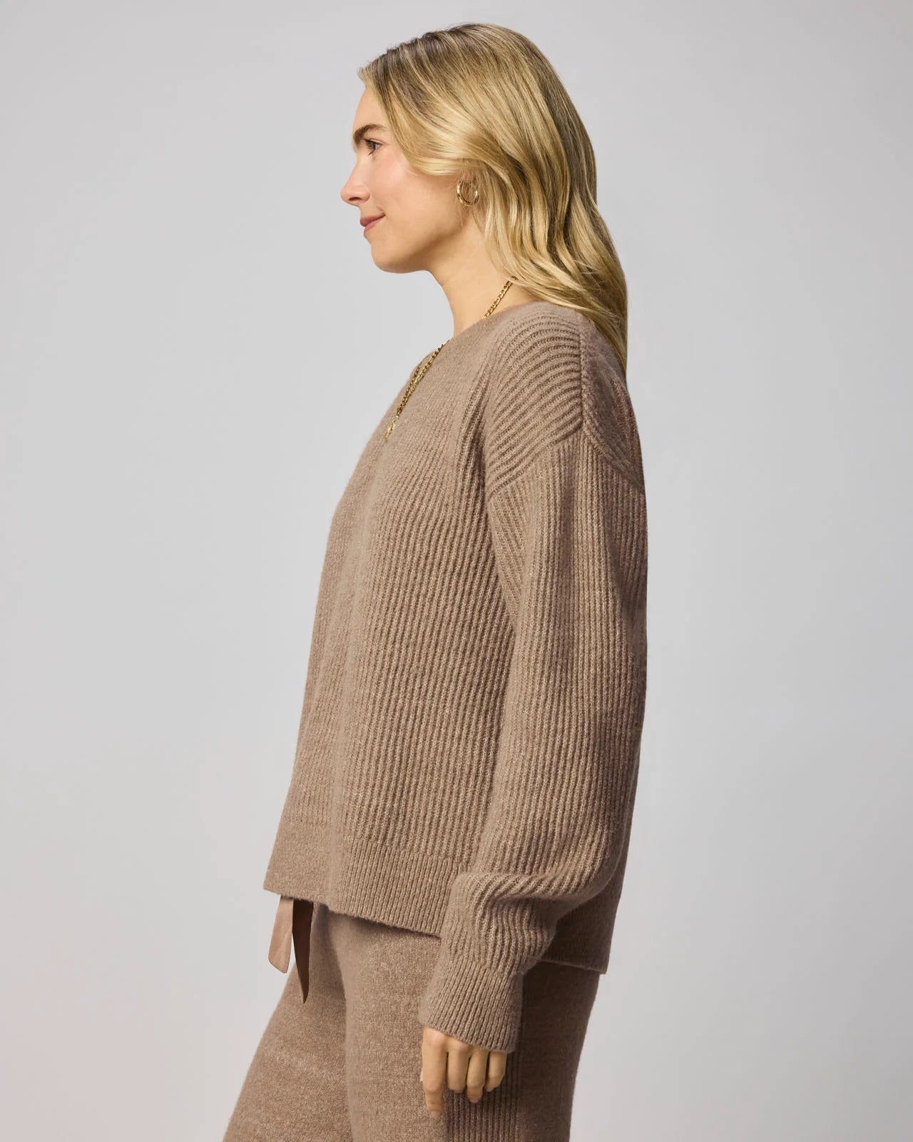 Woman wearing a brown ribbed sweater against a plain background