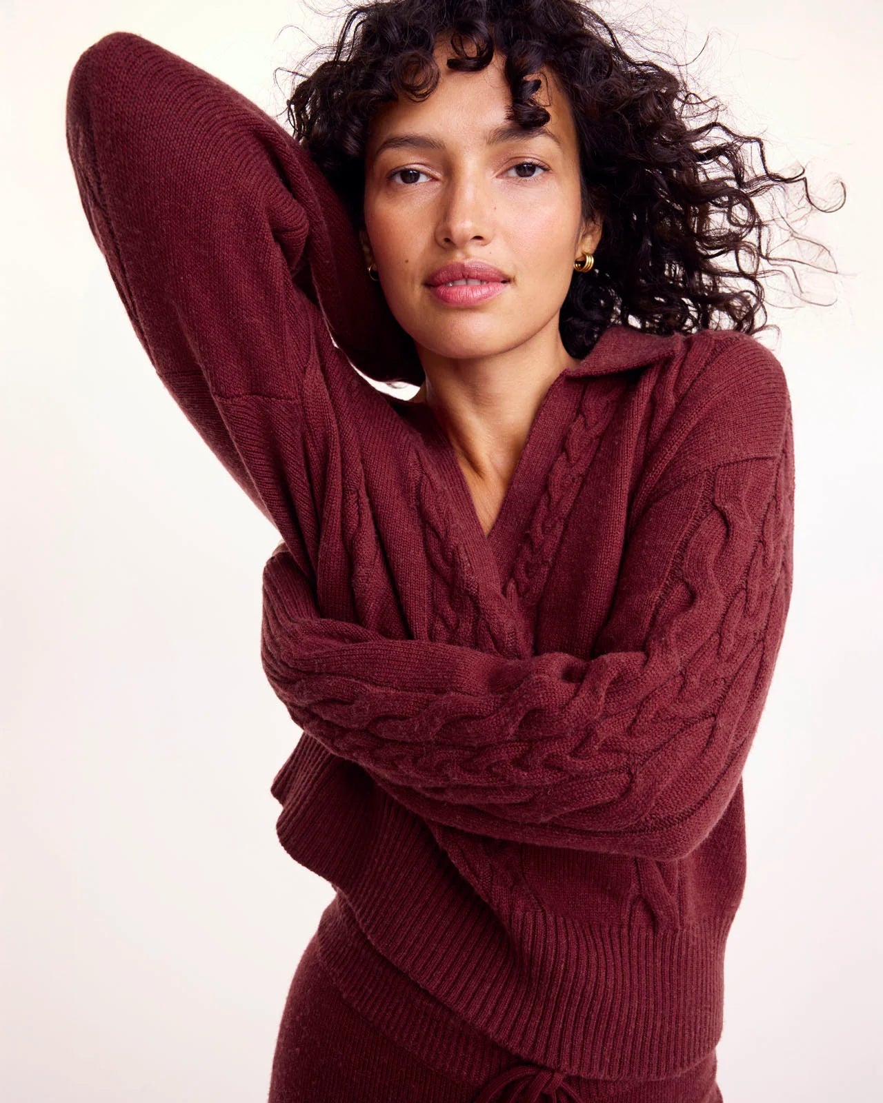 Woman wearing a burgundy cable knit sweater against a plain background