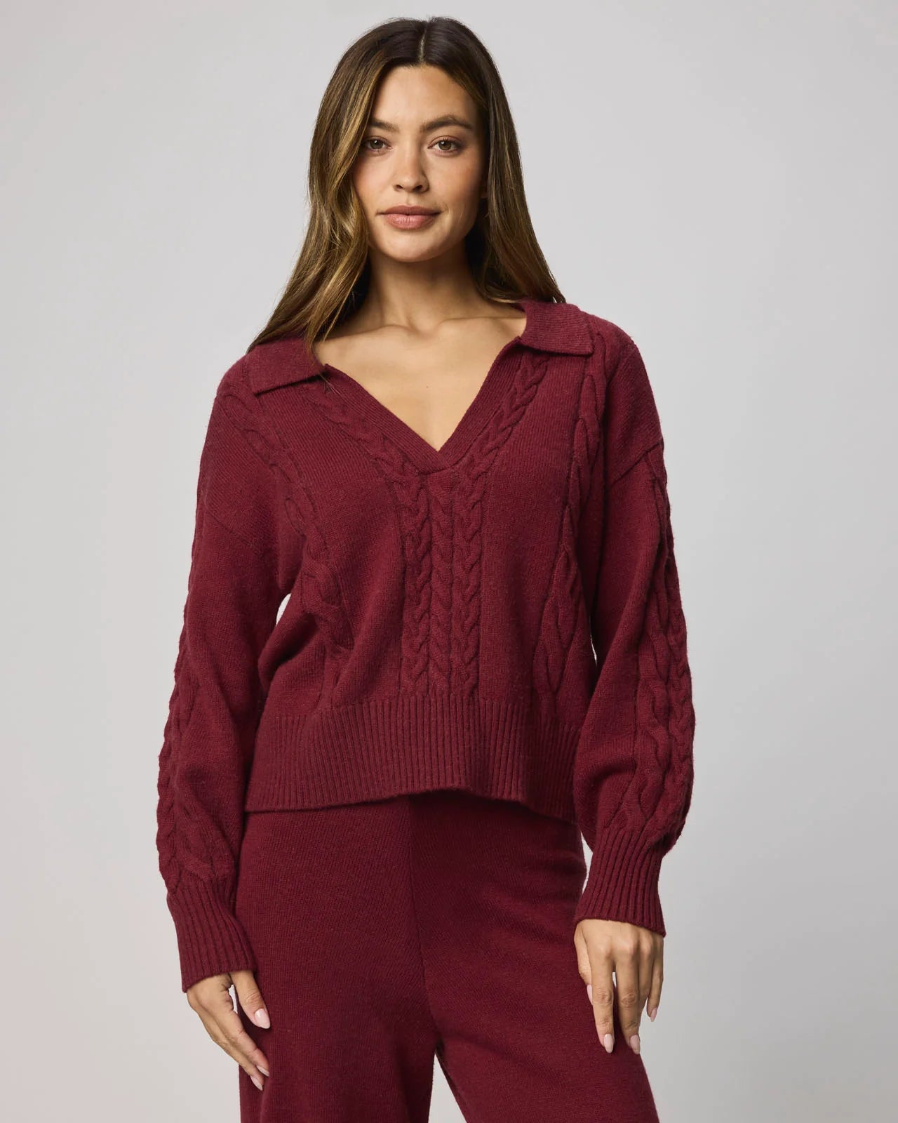 Woman wearing a burgundy sweater and pants against a plain background
