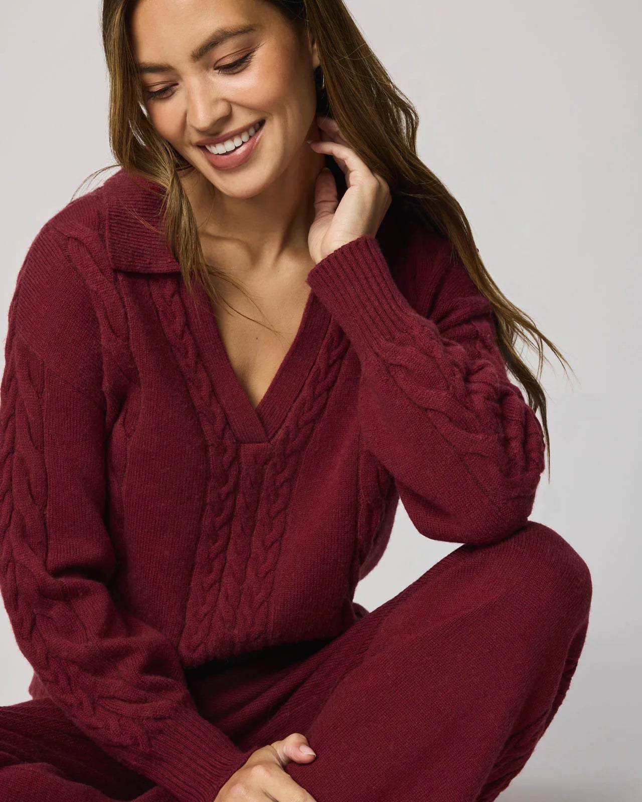 Woman wearing a burgundy cable knit sweater and pants against a plain background