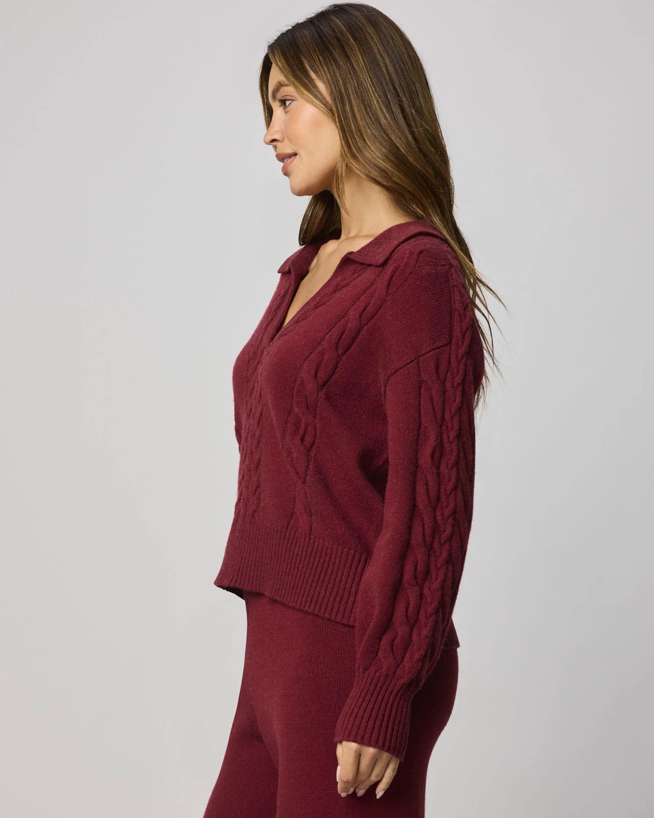 Woman wearing a burgundy cable knit sweater and pants on a plain background