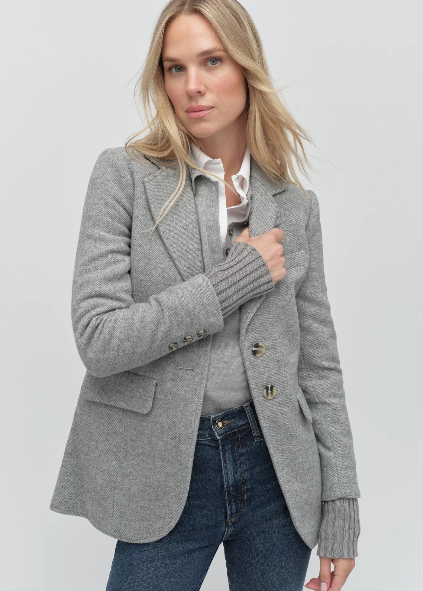 Woman wearing a gray blazer over a white shirt and blue jeans on a light gray background