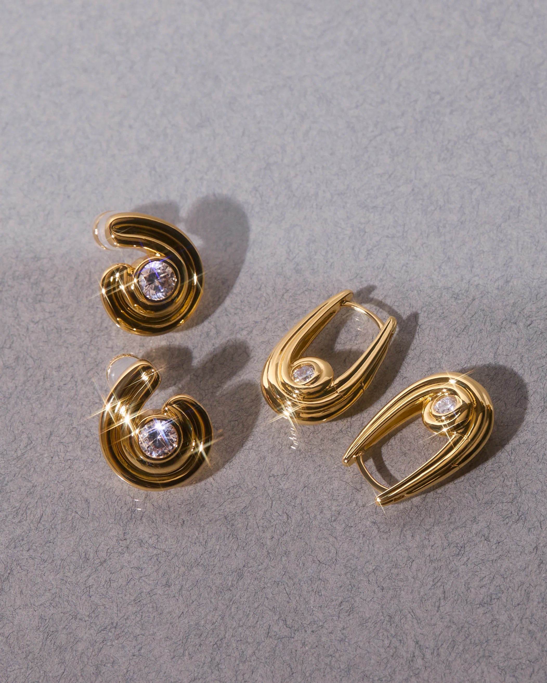 Gold hoop earrings with gemstones on a gray background