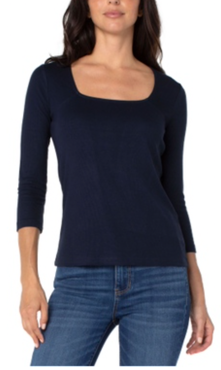 Woman wearing a navy long-sleeve top and blue jeans on a white background