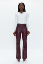 Person wearing a white long-sleeve top and burgundy leather pants on a white background