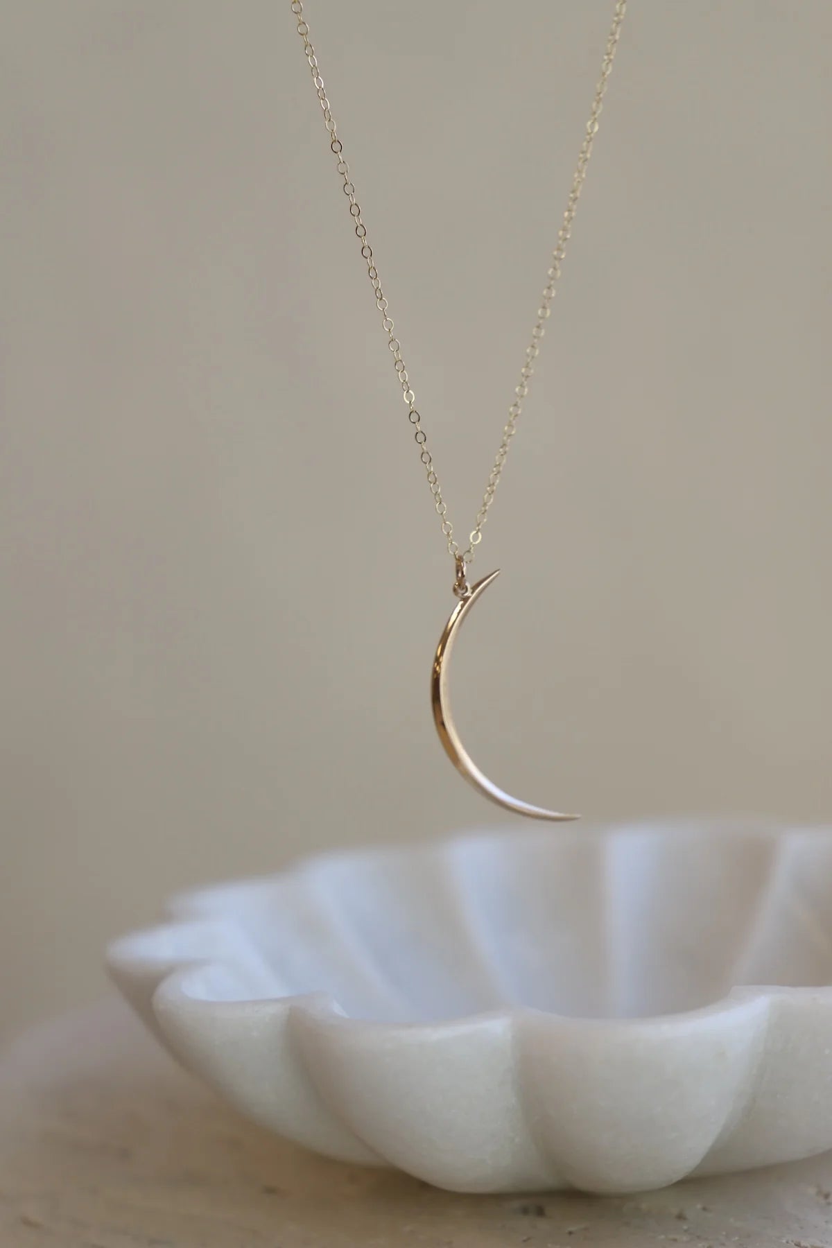 Gold crescent moon necklace on a white dish with a neutral background