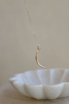 Gold crescent moon necklace on a white dish with a neutral background