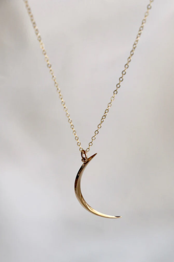 Gold crescent moon necklace on a light gray background