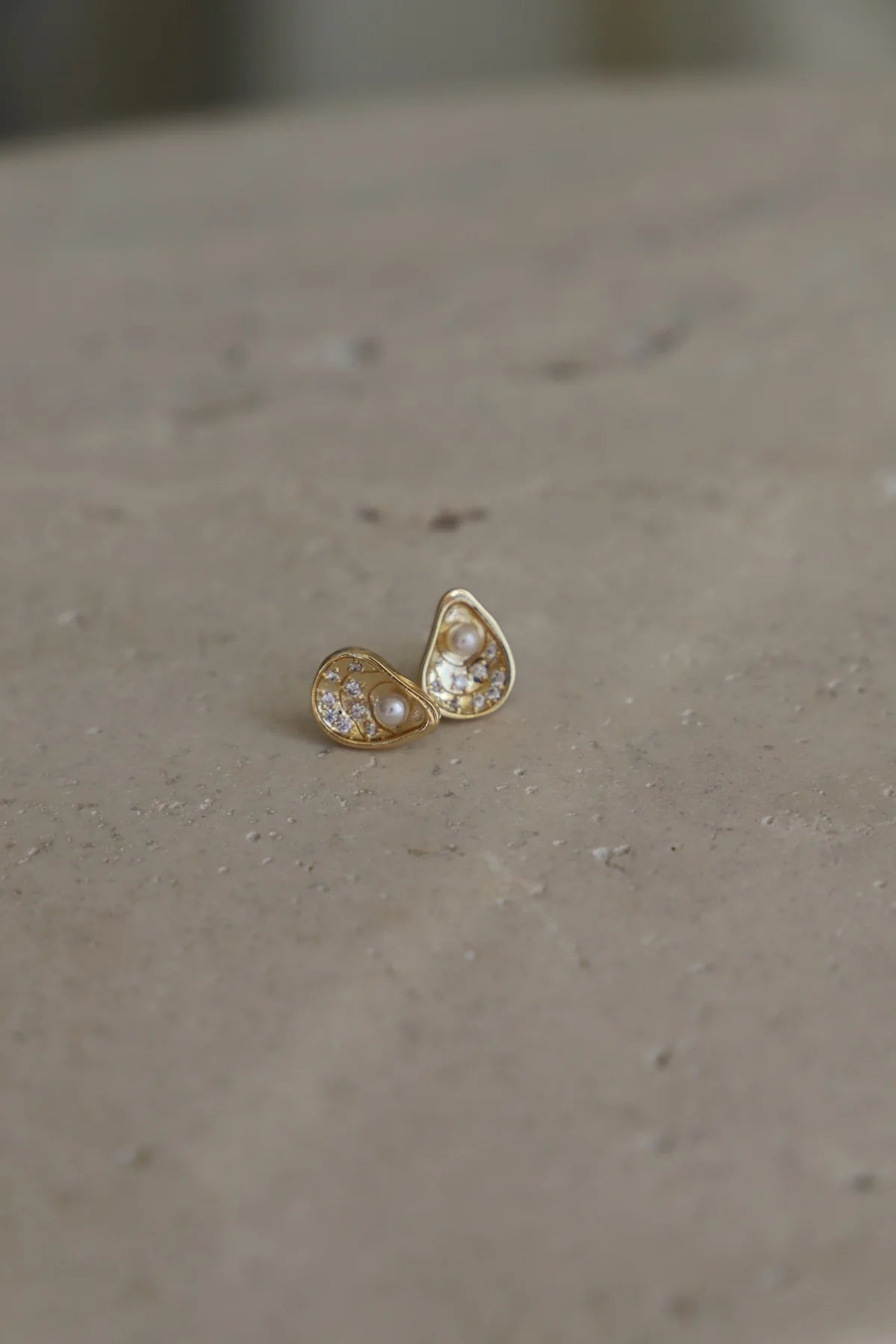 Gold earrings with a pearl-like center on a beige surface