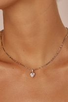 Necklace with a heart-shaped pendant on a person's neck against a neutral background