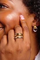 Close-up of a person with gold rings and earrings, covering one eye with their hand.